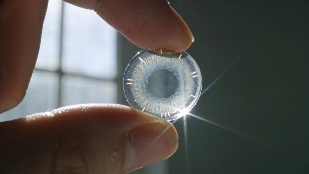 Holding a clear contact lens against bright window light to check edge curvature and microscopic orientation markings.